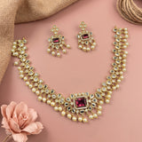 Gold-plated Indian Kundan jewelry set featuring a necklace, earrings, and a matching ring, decorated with clear crystals and pink gemstones, arranged on a dusty pink background with decorative props.
