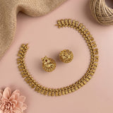 Gold-toned jewelry set arranged on a soft pink background, including a necklace, matching earrings, burlap fabric, twine, and a pink flower.