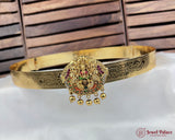 Gold belt with decorative pendant on a white surface with wooden background