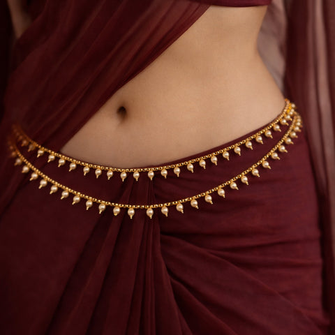 Maroon saree with a gold waist belt featuring pearl-like stones.