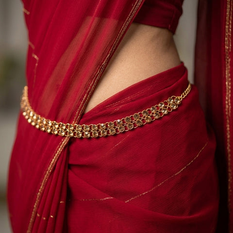 Red saree with a gold belt against a neutral background