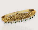 Gold headband with intricate designs and green beads on a light gray background