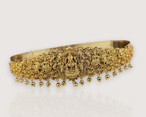 Gold headband with intricate designs and dangling beads on a light background