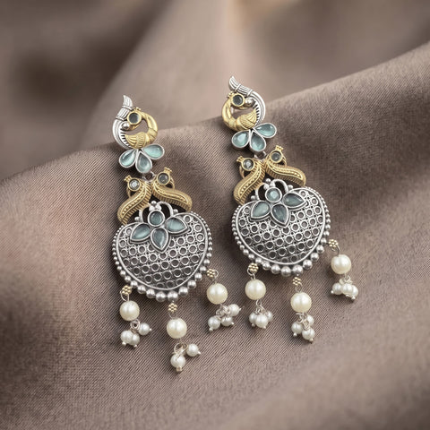 A pair of ornate silver-toned and gold-toned jhumka earrings with light blue enamel details and dangling white pearl beads, displayed on draped brown fabric.