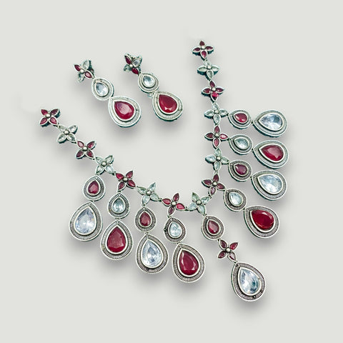 Jewelry set with necklace and earrings featuring red and clear gemstones on a light gray background