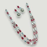 Jewelry set with necklace and earrings featuring red and blue gemstones on a light gray background