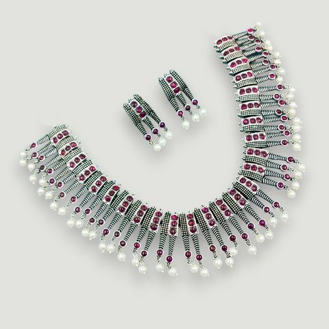 Necklace and earrings set with pearls and red gemstones on a light gray background