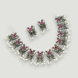 Ornate silver necklace with red gemstones and matching earrings on a light gray background