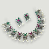 Ornate silver necklace with green and red gemstones on a light gray background