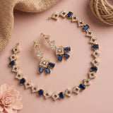 Gold-tone jewelry set with blue rectangular stones and clear rhinestone square links, arranged on a pink background with burlap, twine, and a pink flower.