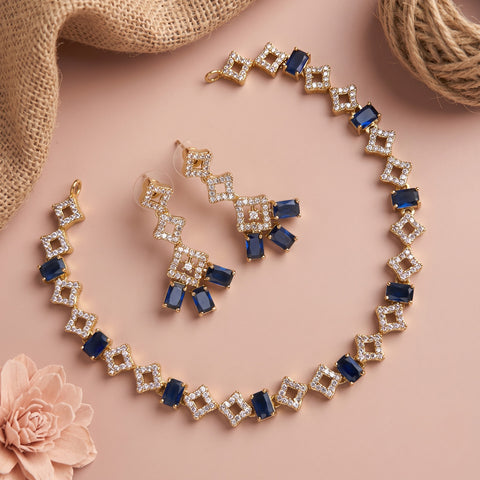 Gold-tone jewelry set with blue rectangular stones and clear rhinestone square links, arranged on a pink background with burlap, twine, and a pink flower.