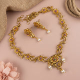 Gold-toned floral jewelry set with a matching necklace and earrings, featuring small pink gemstone accents and dangling white faux pearls, arranged on a soft pink background with burlap and a pink flower prop.