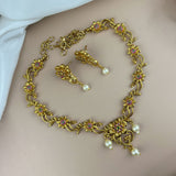 Gold necklace with floral designs and pearl-like beads on a plain background