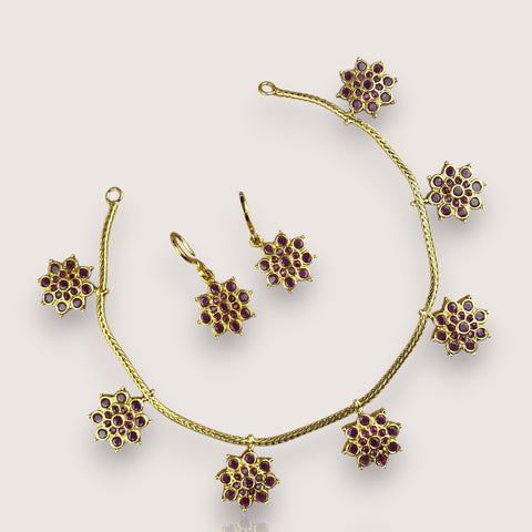 Gold jewelry set with floral designs and red stones on a white background