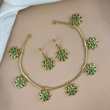 Gold necklace and earrings with green gemstones on a beige surface