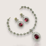 Jewelry set with necklace and earrings featuring red gemstones on a light pink background