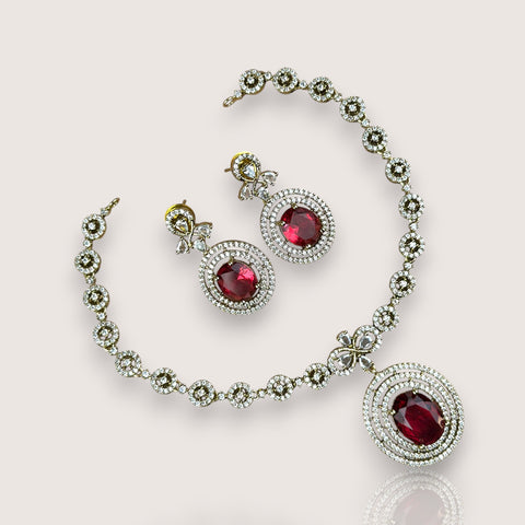 Jewelry set with necklace and earrings featuring red gemstones on a light pink background
