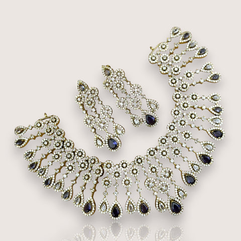 Ornate necklace and earrings with blue gemstones on a light gray background