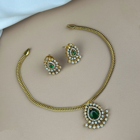 Gold necklace with green gemstones and matching earrings on a beige surface