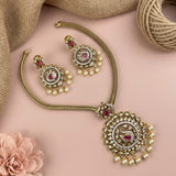Gold-toned Indian traditional jewelry set featuring a necklace and matching earrings with intricate filigree, white faux pearls, and pink gemstone accents, arranged on a soft pink background with burlap and a flower prop.