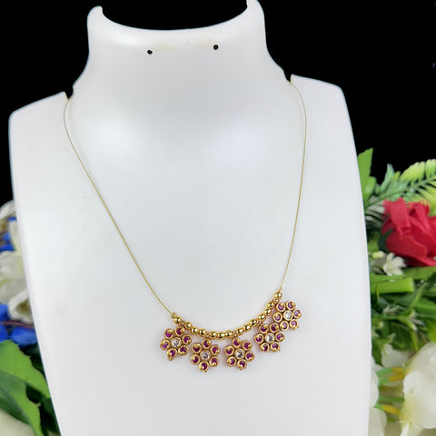 Gold necklace with red stones on a mannequin bust against a floral background