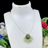 Gold necklace with green and white pendant on a mannequin against a floral background