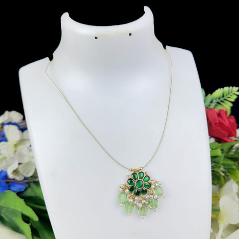 Gold necklace with green and white pendant on a mannequin against a floral background