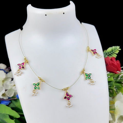 Delicate gold necklace with green and pink pendants on a white mannequin bust against a floral background.