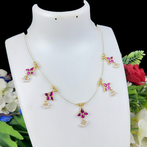 Gold necklace with pink and purple floral pendants on a white mannequin bust with flowers in the background.