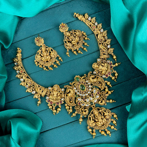 Gold jewelry set with necklace and earrings on a teal fabric background