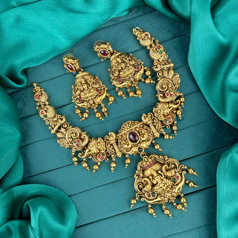 Ornate gold necklace and earrings on a teal fabric background
