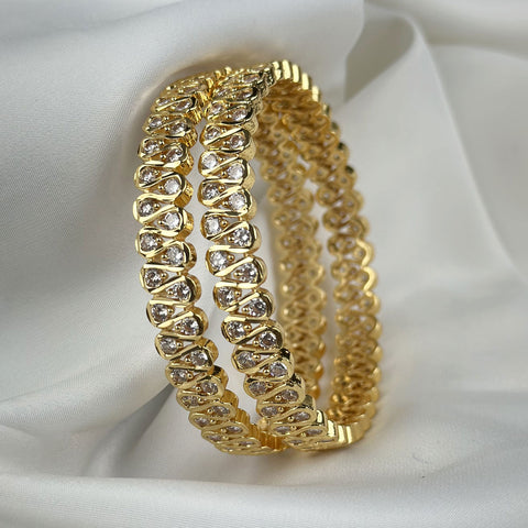Gold bracelets with diamond-like stones on a white fabric background
