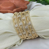 Gold bangles with leaf patterns on a white fabric background