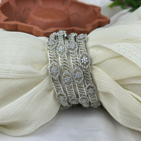 Silver bangles with intricate designs on a white fabric background
