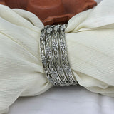 Set of silver bangles with intricate designs on a white fabric background