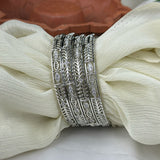 Set of silver bangles with intricate designs on a white fabric background