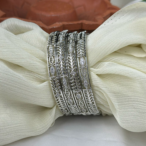 Set of silver bangles with intricate designs on a white fabric background