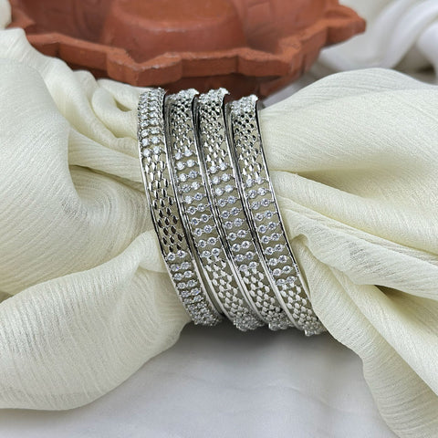 Set of silver bangles on a white fabric with a terracotta dish in the background
