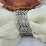 Silver bracelets on a white fabric with a terracotta dish in the background