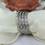 Set of silver bangles with intricate designs on a white fabric background