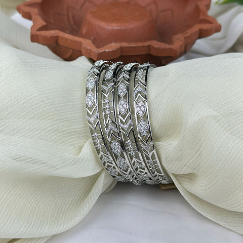 Set of silver bangles with intricate designs on a white fabric background