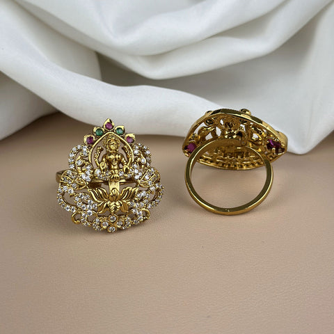 Two ornate gold rings with gemstones on a beige surface with white fabric in the background