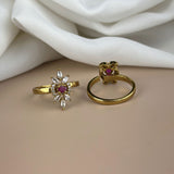 Two gold rings with gemstones on a beige surface with white fabric in the background