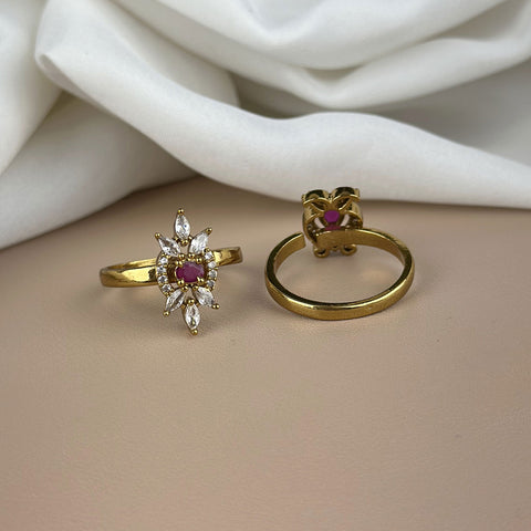 Two gold rings with gemstones on a beige surface with white fabric in the background