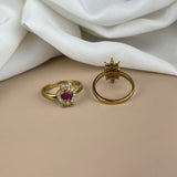 Two gold rings with gemstones on a beige surface with white fabric in the background