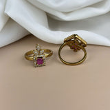 Two gold rings with gemstones on a beige surface with white fabric in the background