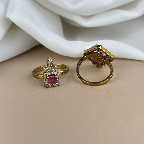 Two gold rings with gemstones on a beige surface with white fabric in the background