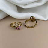 Gold ring with purple gemstones on a beige surface with white fabric in the background