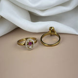 Gold ring with a red gemstone and gold hoop earring on a white fabric background