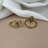 Gold ring with gemstones and gold hoop earring on a beige surface with white fabric